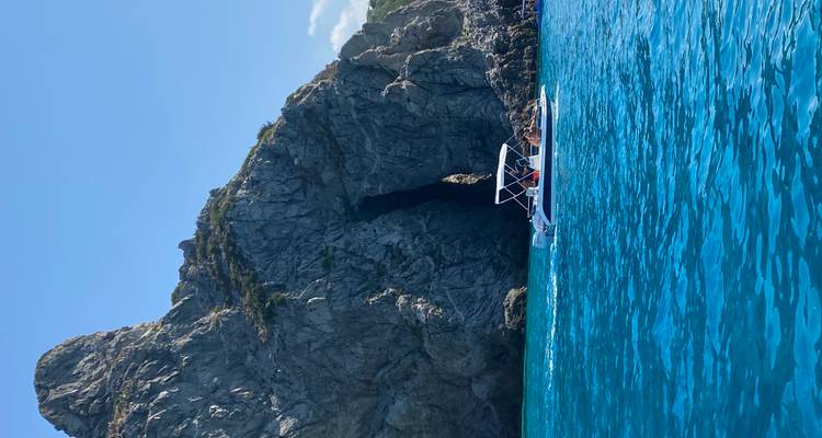 Un petit bateau à moteur glissant sur une eau cyan éclatante à côté d'une falaise escarpée avec une étroite grotte marine.