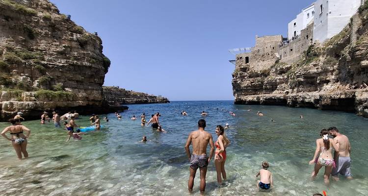 Urlauber schwimmen in smaragdgrünen Gewässern zwischen hohen Kalksteinfelsen unter historischen Gebäuden.