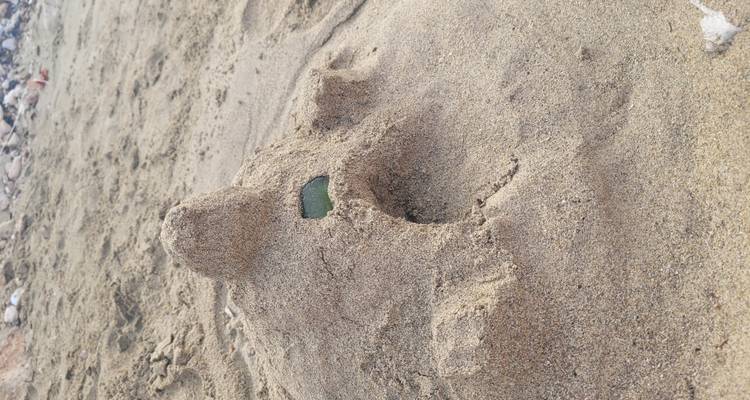 Kleine Sandburg mit Tunnel und Glasscherben-Fenster auf einem Sandstrand.