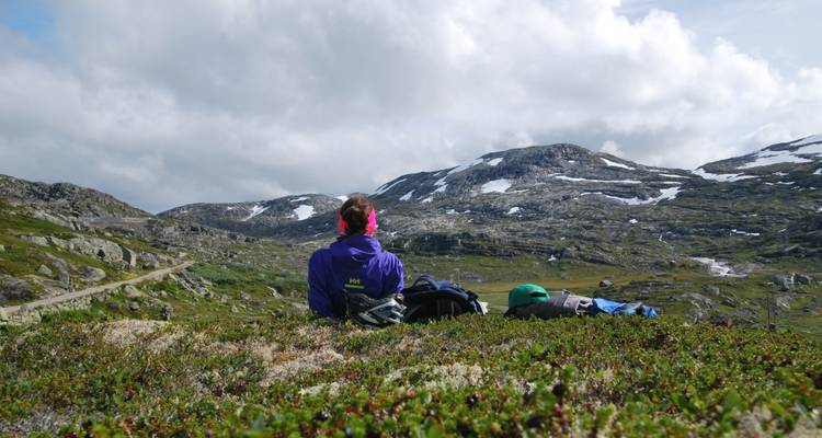 Un voyageur s'allonge sur la lande alpine en contemplant les pics rocheux striés de neige de fin de saison.