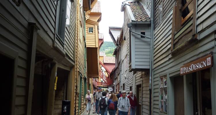 Ruelle étroite en bois de Bryggen avec des touristes marchant entre les anciens entrepôts penchés.