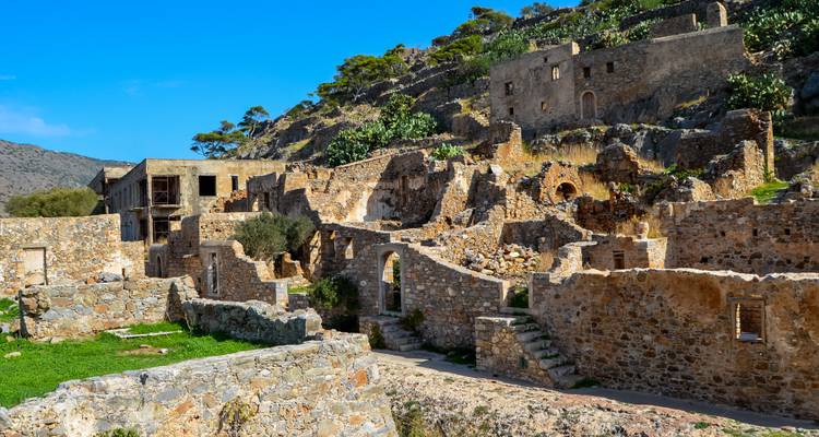 Stone ruins of a deserted village set on a rocky hillside under a bright blue sky on Spinalonga.