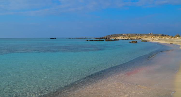 Serene stretch of shallow, crystal-clear sea with subtle pink sand and a distant headland.