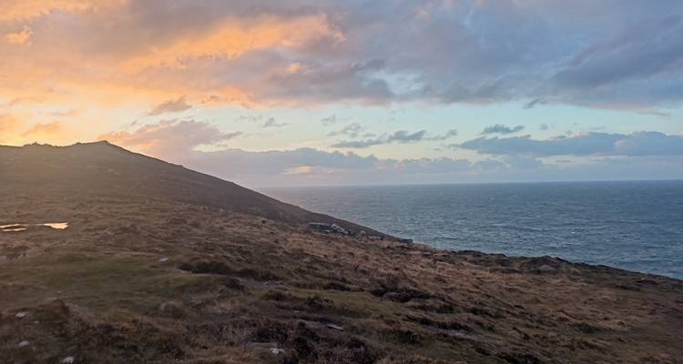 Côte atlantique au coucher du soleil avec des nuages luminescents au-dessus d'un promontoire balayé par les vents et la mer ouverte.