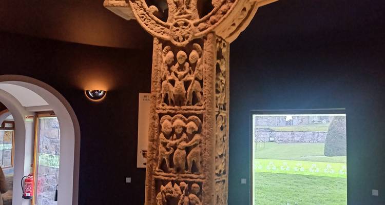 Une croix celtique chrétienne primitive richement sculptée exposée à l'intérieur d'une galerie de musée faiblement éclairée.