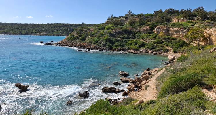 Clifftop view of turquoise bay bordered by green shrubs and rocky terrain