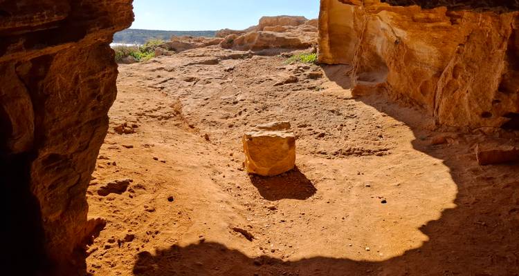 Sun-lit reddish cave interior opening to rocky terrain outside