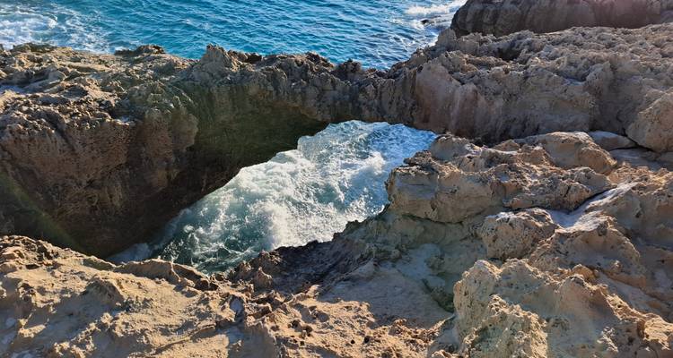 Sea water surging beneath a natural rock arch viewed from above