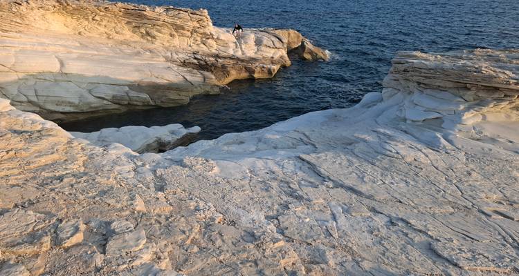Person standing on layered white rock formations above dark blue sea