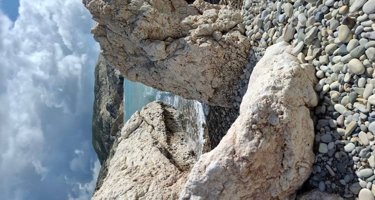 Pebble beach framed by large pale rocks with turquoise water and mountains beyond