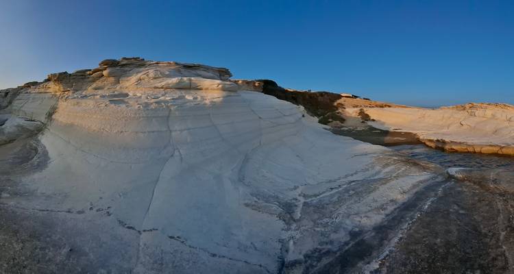 Wide view of smooth white layered rock hill under clear blue sky