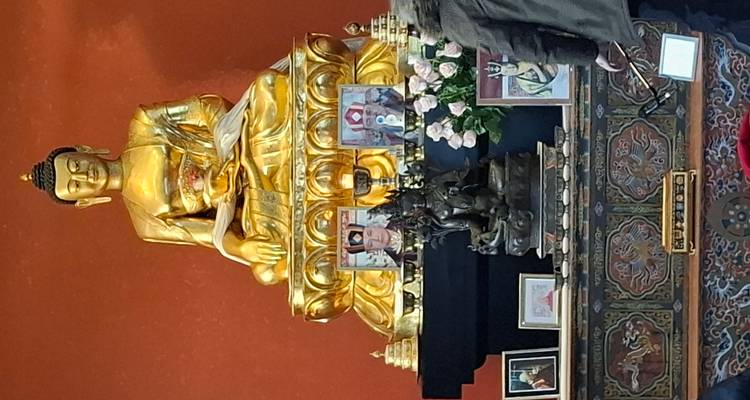 Statue de Bouddha assis en or sur un autel orné avec des offrandes et des visiteurs.