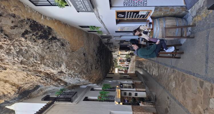 Rue à Setenil de las Bodegas construite sous un immense surplomb rocheux avec des clients attablés à une table en tonneau.
