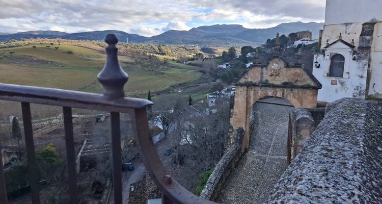 Vue sur la campagne vallonnée et les montagnes, visible à travers une arche en pierre et une balustrade en fer à Ronda.