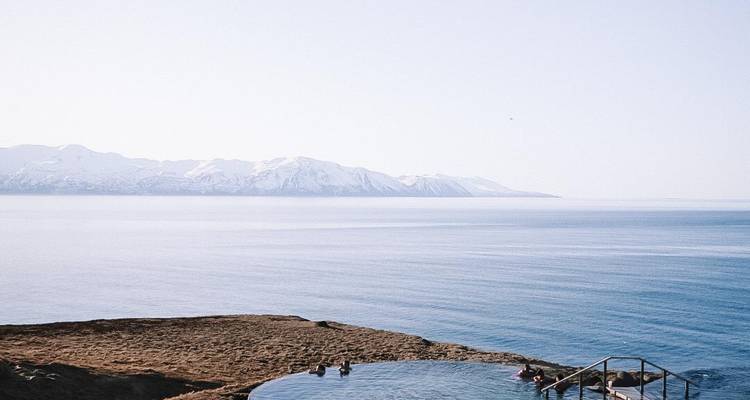 La piscine thermale à débordement surplombe un fjord tranquille avec des montagnes enneigées sous un ciel dégagé.