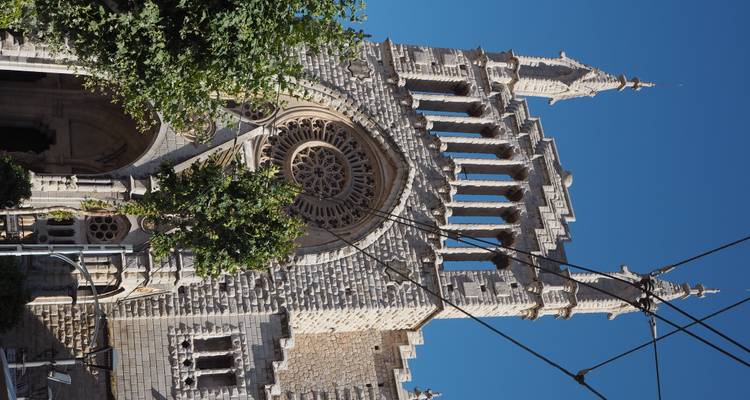 Façade en pierre de la Cathédrale de Sóller avec rosace et tours sous un ciel bleu dégagé et des câbles aériens.