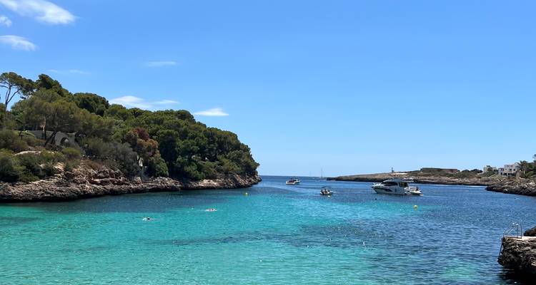 Crique turquoise encadrée par des promontoires rocheux avec des yachts et des baigneurs profitant des eaux cristallines de la Méditerranée.