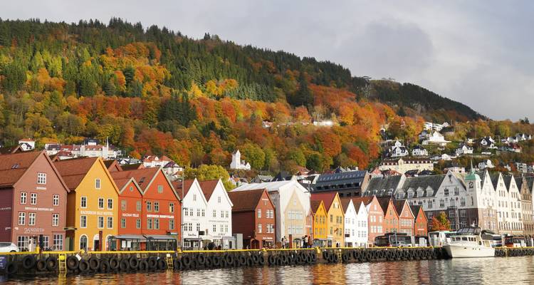 Les entrepôts en bois colorés bordent le front de mer de Bryggen avec des collines forestières automnales qui s'élèvent en arrière-plan et leurs reflets dans le port.