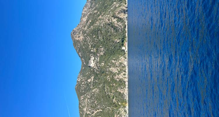 Steep, rocky mountains rise from deep blue water under a pristine sky, viewed from offshore.