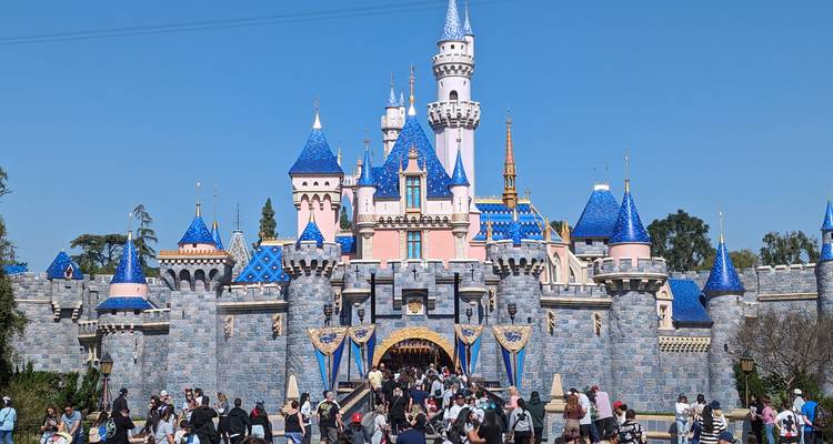 Cour avant bondée du château de Disneyland sous un ciel bleu dégagé avec des familles entrant dans l'attraction magique.
