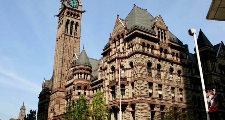 Vue panoramique de l'ancien hôtel de ville de Toronto avec sa tour horloge se détachant sur un ciel bleu clair.