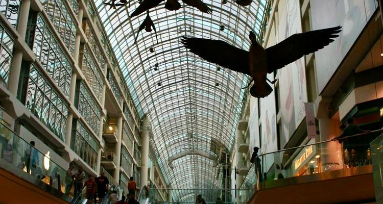 Intérieur du CF Toronto Eaton Centre avec toit en verre arqué et sculptures d'oies du Canada suspendues au-dessus des clients.