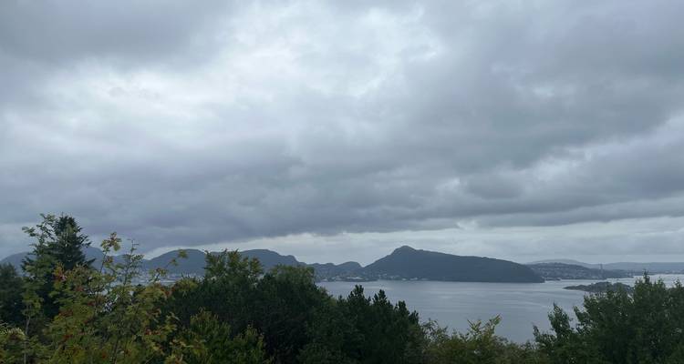 Vue panoramique couverte sur un fjord vers des collines boisées lointaines et des nuages bas.