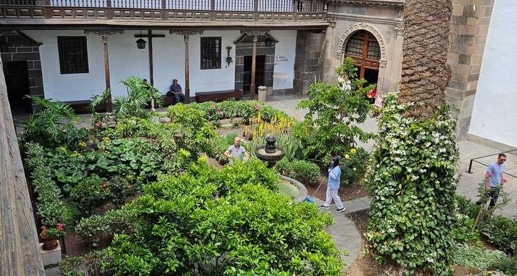 Jardin de cour feuillu avec une fontaine centrale à l'intérieur d'un bâtiment historique, des visiteurs se promenant.