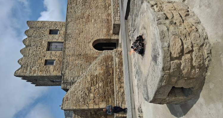 Autel de feu en pierre avec de faibles flammes devant un bâtiment historique de style forteresse, un homme assis à proximité