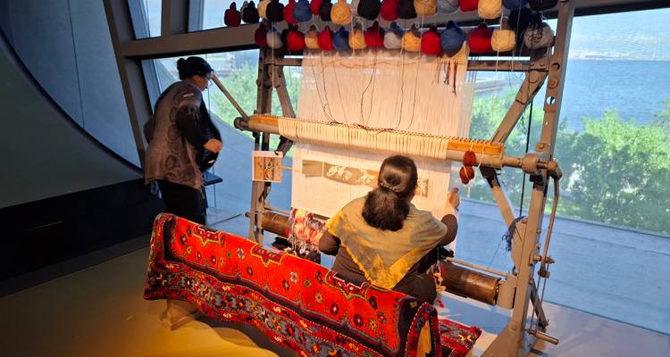 Les tisseurs de tapis traditionnels travaillant sur un grand métier à tisser dans une galerie de musée surplombant la mer