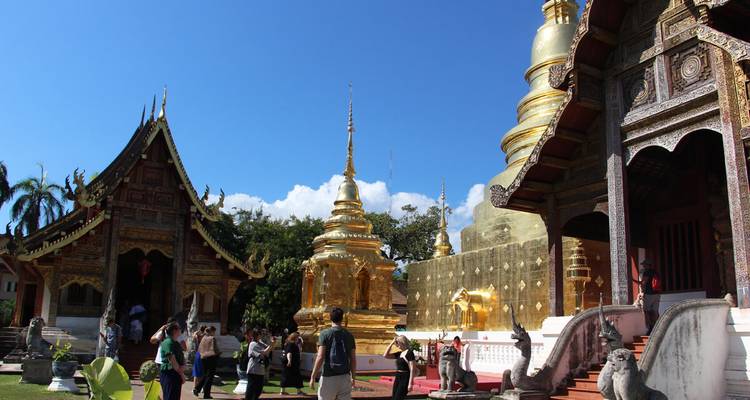 Stupas dorados y viharn de madera ornamentada de un complejo de templos de Chiang Mai lleno de visitantes