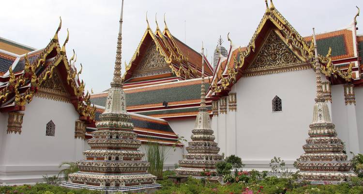 Stupas altos con azulejos intrincados elevándose junto a muros de templo blancos y un pequeño jardín