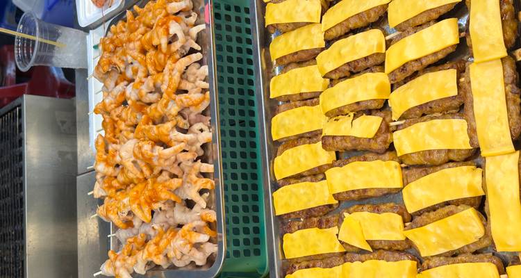 Street food stall displaying skewered meats glazed with sauce and cheese slices.