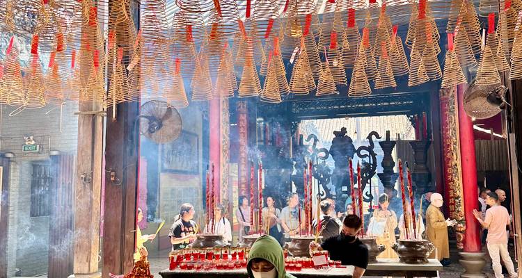 Temple interior filled with spiral incense coils hanging overhead and visitors offering prayers amid smoke.