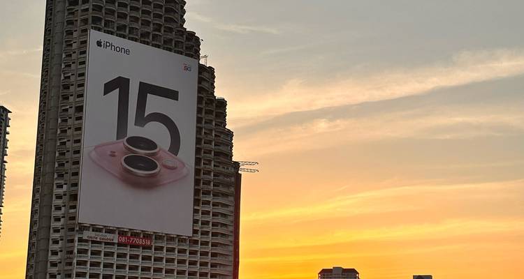 Edificio de gran altura con un enorme anuncio del iPhone 15 recortado contra un vibrante cielo al atardecer.