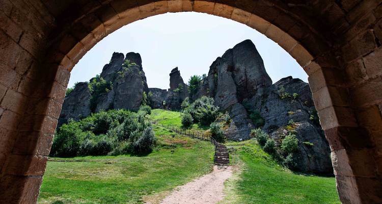 Vue à travers une arche en pierre vers les rochers escarpés de Belogradchik et un sentier sinueux.