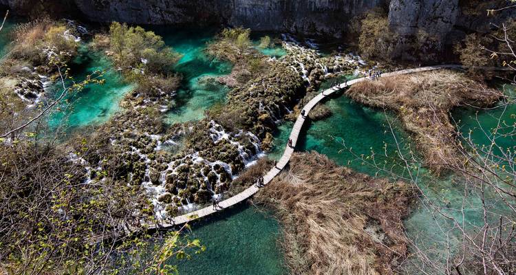 Luchtfoto van een kronkelend houten looppad dat over smaragdgroene poelen en travertijn watervallen loopt.