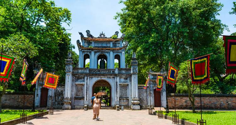 Gran puerta de piedra del Templo de la Literatura rodeada de banderas cuadradas de colores brillantes y árboles.