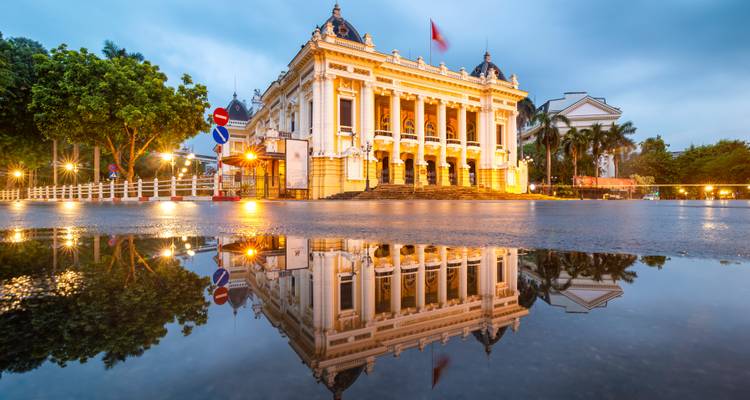Casa de ópera de estilo francés elegante iluminada al atardecer, perfectamente reflejada en un charco de lluvia.