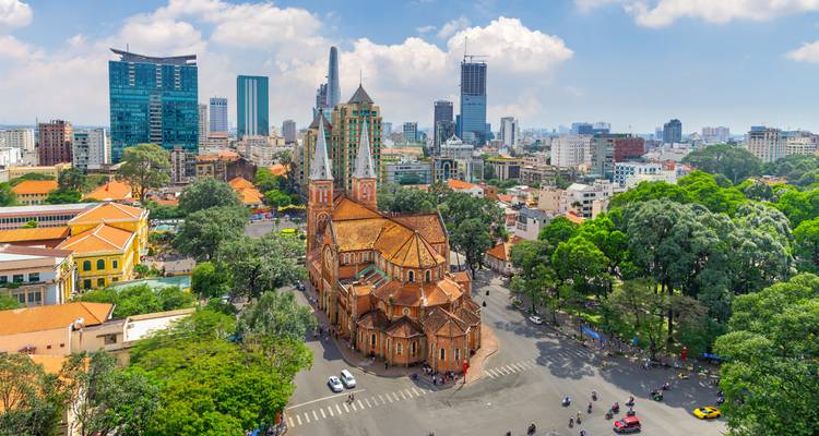 Vista aérea de la Catedral Basílica de Notre-Dame de Saigón enmarcada por rascacielos modernos y calles arboladas.