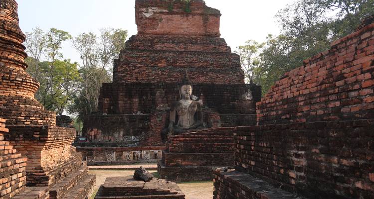Zerstörter Ziegeltempel mit einer sitzenden Buddha-Statue, umrahmt von alten Mauern unter diffusem Sonnenlicht.