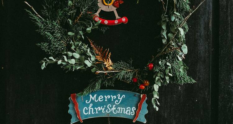 Rustic wreath with greenery and berries hanging on a dark door with a 'Merry Christmas' sign