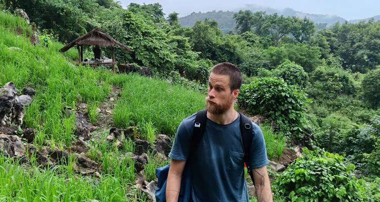 Mannelijke trekker pauzeert op een weelderig bergpadpad met uitzicht op mistige, met jungle bedekte bergen.