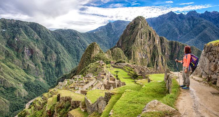 Ein Wanderer mit einem Rucksack bewundert die Panoramaaussicht auf die Ruinen von Machu Picchu von einem Bergpfad aus.