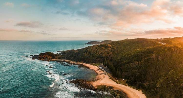 Vista aérea costera del promontorio boscoso y playa arenosa apartada a la hora dorada