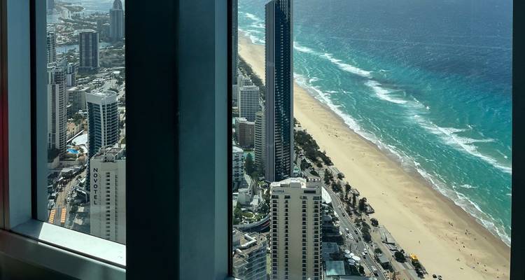 Aerial coastal skyline of Surfers Paradise and long golden beach seen through a tower window.