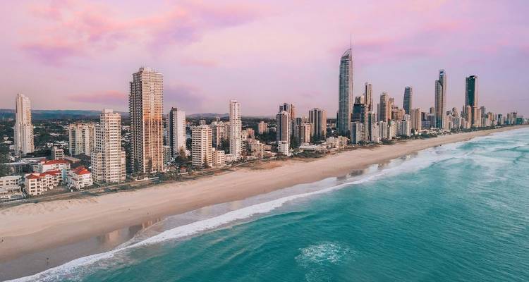 Drone image of Gold Coast skyscrapers lining a pastel-coloured sunset beach.