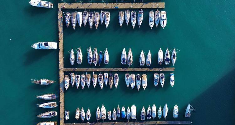 Top-down view of marina docks neatly lined with sailboats on emerald water.