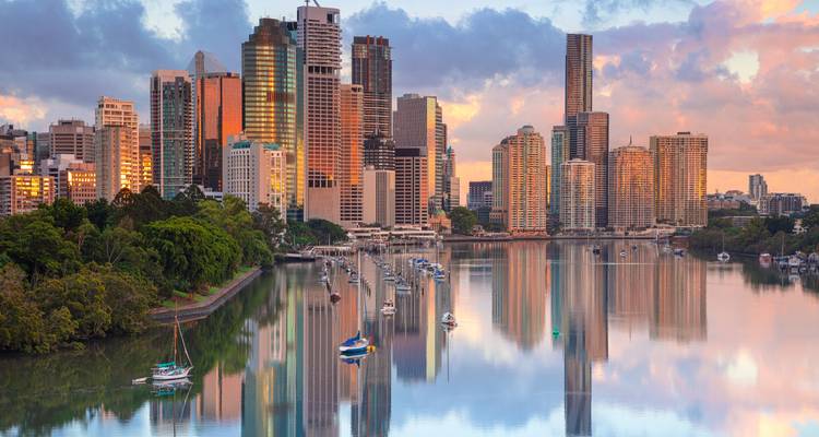 Moderne Brisbane skyline die weerspiegeld wordt in de Brisbane River met aangemeerde zeilboten tijdens een kleurrijke dageraad.