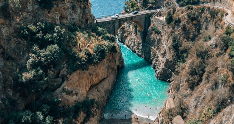 Turquoise baai onder een stenen brug aan de Amalfi Kust met zwemmers onder steile kliffen.